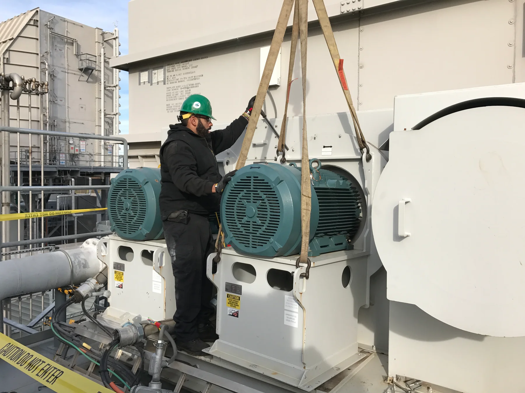 Technician guiding a suspended motor at an industrial facility